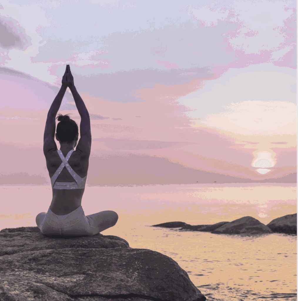 Yogadame auf einem Stein vor einem Sonnenuntergang am Strand