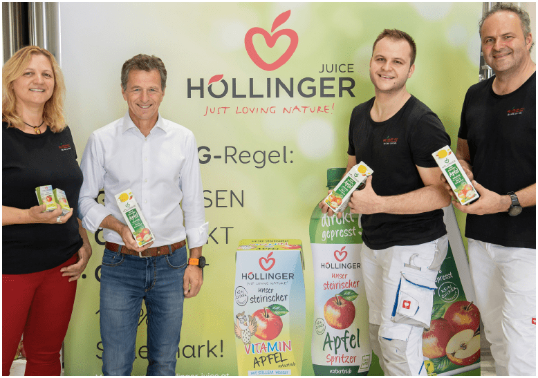 Vier Personen vor einem Werbeschild von HÃ¶llinger mit einer Apfelsaft-Packung in der Hand